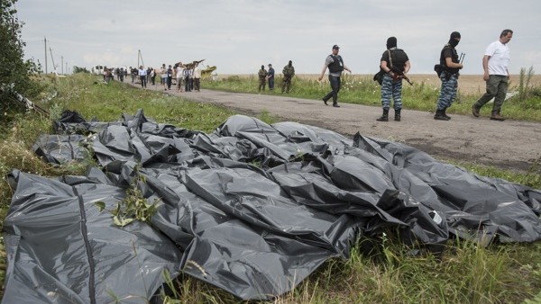 Pro-Russian fighters walk on a road with victims' bodies lying in bags by the side at the crash site of a Malaysia Airlines jet near the village of Hrabove, eastern Ukraine, Saturday, July 19, 2014. Ukraine accused Russia on Saturday of helping separatist