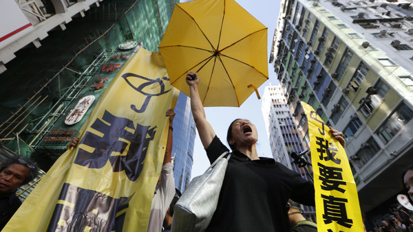 In this Tuesday, Nov. 25, 2014 photo, a pro-democracy protester chants umbrella and a yellow banner at an occupied area before the barricade is removed in Mong Kok district of Hong Kong. Hong Kong authorities on Tuesday began clearing away some barricades