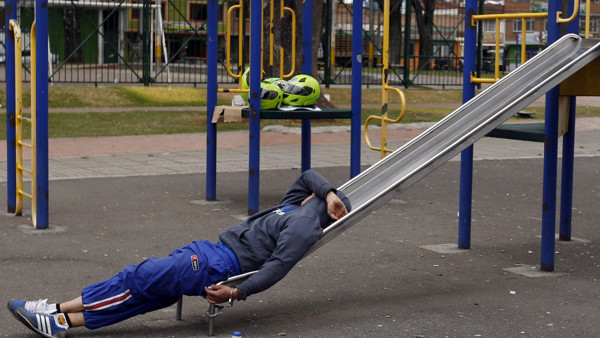 FILE - In this Sept. 11, 2014 file photo, a detainee rests, handcuffed to a slide, at a children's playground in a public park in Bogota, Colombia. Authorities have been holding some crime suspects in a public park in western Bogota's La Granja neighborho