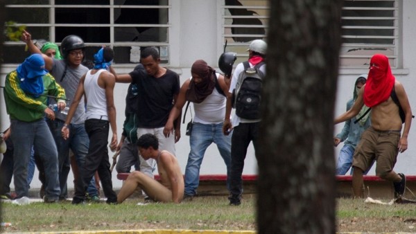 FILE - In this April 3, 2014 file photo, government supporters beat a naked opposition student as he's forced to sit on the ground inside of the Central University of Venezuela, UCV, during an anti-government protest in Caracas, Venezuela. Students attemp